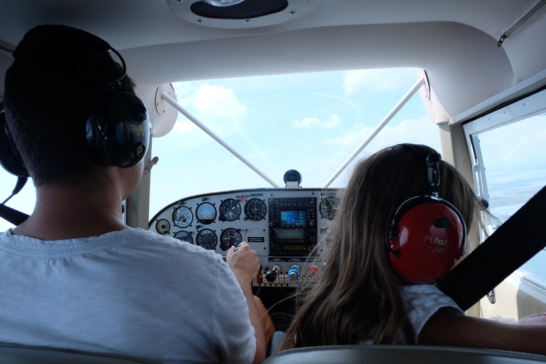 Dans le cockpit du Maule en vol, une enfant au casque rouge à la place de droite